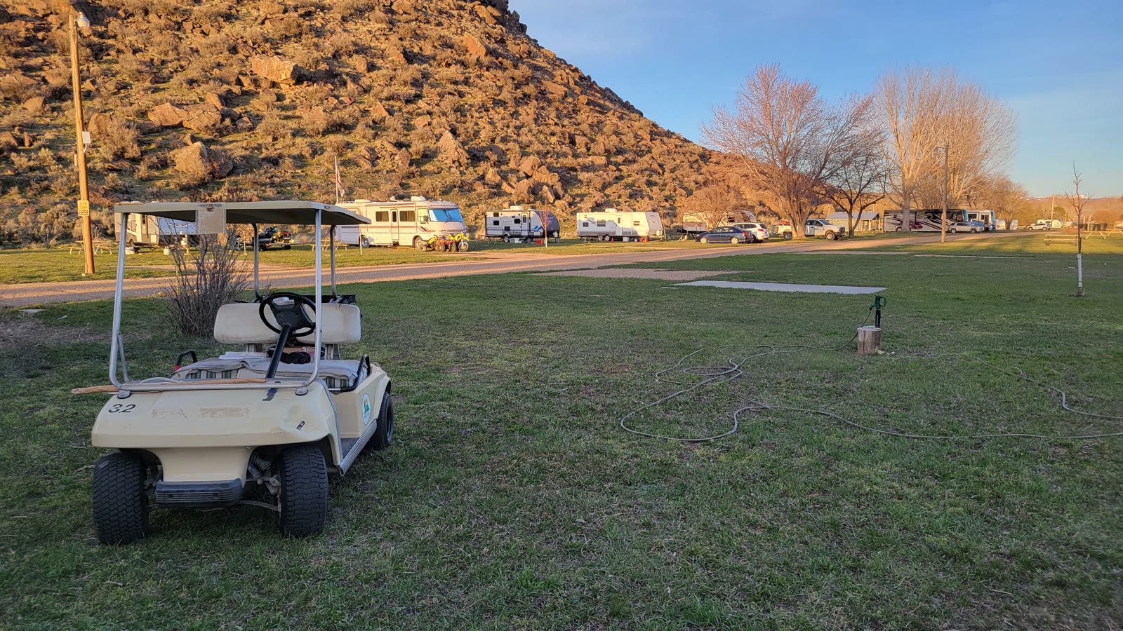 Grassy RV sites at Sunny Ridge RV Park beneath the rocky butte at golden hour